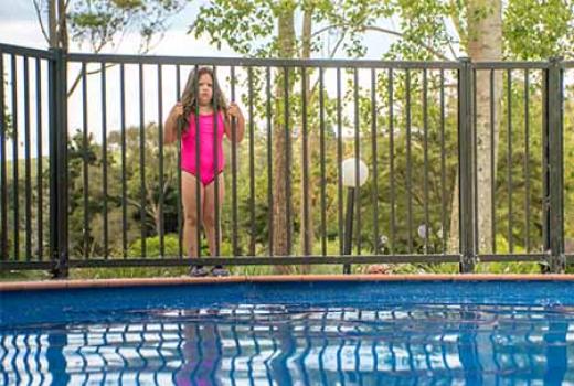 Girl in bathers looking at pool through a fence